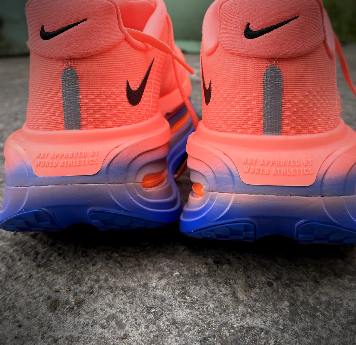 Heel view of the Nike Vomero Premium, showing the coral-to-blue midsole fade, reflective heel strips and a moulded "Not approved by World Athletics" marking